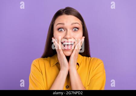 Ritratto fotografico di donna sorridente che tocca le guance stupite isolate su sfondo color viola pastello Foto Stock