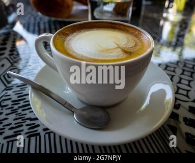 primo piano di una tazza di cappuccino su un piatto con un cucchiaio sul tavolo in un caffè Foto Stock