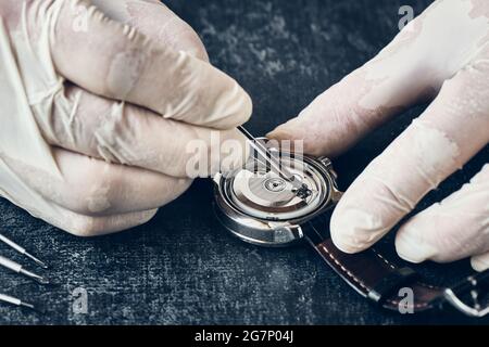 Dettagli del lavoro orologiaio con pinzette in guanti in vinile, macro, riparazione orologio da polso Foto Stock