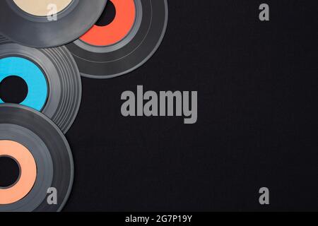Dischi in vinile singolo multicolore da 7 pollici su sfondo nero posizionati nell'angolo superiore sinistro con spazio vuoto per il testo. Vista dall'alto in piano. Retrò Foto Stock