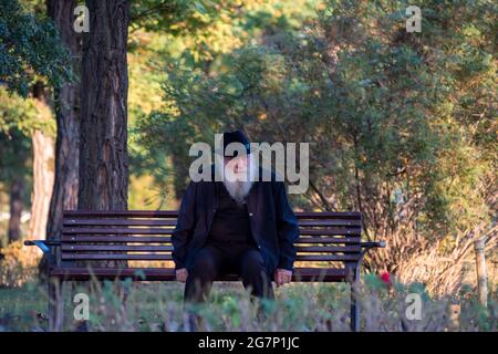 Timisoara, Romania - 10 ottobre 2020: Uomo seduto su una panchina in un parco. Persone reali. Foto Stock