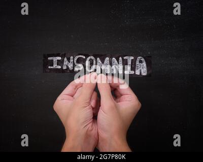 Una persona che tiene un pezzo di carta nero con la parola Insomnia su di esso nelle sue mani. Primo piano. Foto Stock