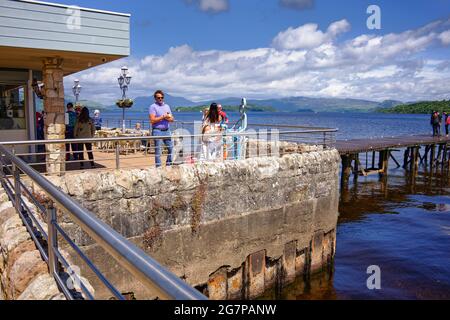 Le persone che godono del sole sulle rive del Loch Lomond presso il caffè di Duck Bay Marina Foto Stock