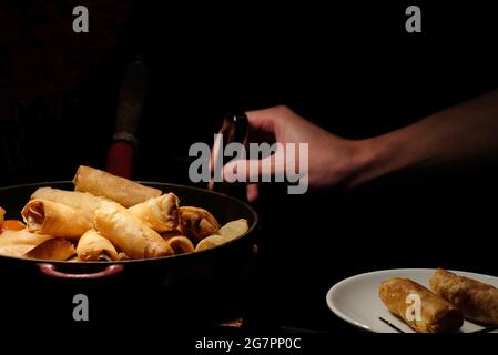 i panini primaverili fritti e profondi si surgono sulla padella su sfondo scuro con la mano, prenderne uno e metterlo in un piccolo piatto Foto Stock