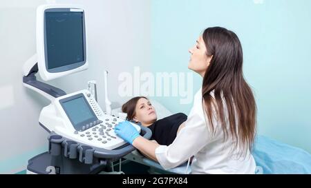 Il medico concentrato della donna conduce la procedura di indagine ecografica alla giovane donna incinta guardando lo schermo nel moderno ufficio dell'ospedale Foto Stock