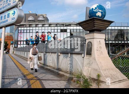 I pedoni passano sopra il Ponte Olimpico vicino al Parco Yoyogi, Tokyo, il 21 giugno 2021. Mentre il ponte faceva parte di un nuovo sistema stradale costruito prima delle Olimpiadi del 1964, i globi in cima alle colonne e i rilievi in pietra a tema olimpico furono aggiunti più di 25 anni dopo. Robert Gilhooly foto Foto Stock