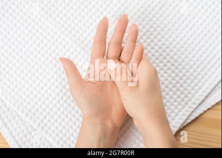 una mano femminile massaggia l'altra mano sdraiata su un asciugamano bianco con il palmo aperto. Closeup mano di persona massaggiare la sua mano dal dolore in una sana con Foto Stock