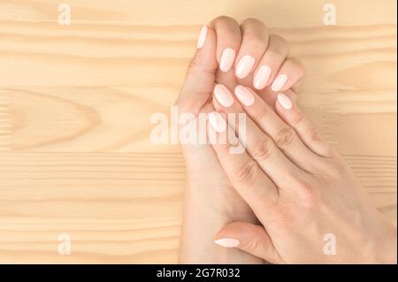 Closeup di una donna in un salone unghie ottenere un manicur. Le mani delle donne con una manicure eccellente sullo sfondo di un tavolo di legno. Rosa chiaro na Foto Stock