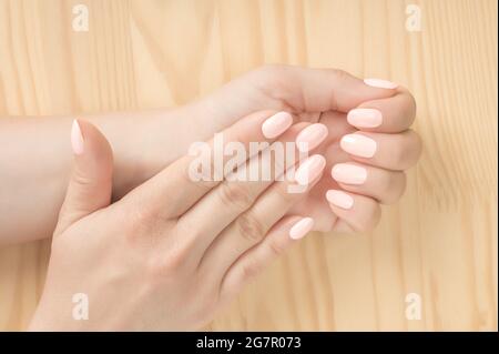 Primo piano di una donna in un salone unghie ottenere un manicur. sfondo di legno. Belle mani di donna curate con unghie rosa bianche. Perfetto, curata Foto Stock