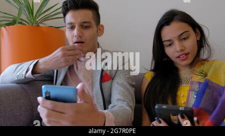 Una coppia di uomini e donne indiane seduti su un divano mentre si usano i telefoni cellulari Foto Stock
