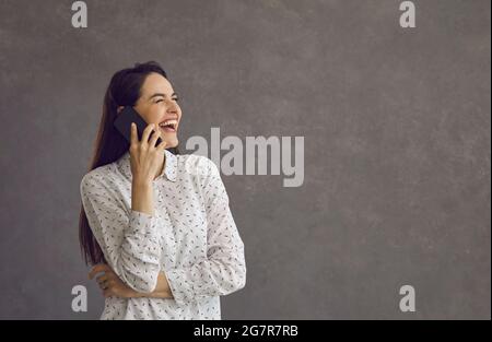 Felice giovane donna gioiosa che ride sinceramente ha una piacevole conversazione su un telefono cellulare. Foto Stock