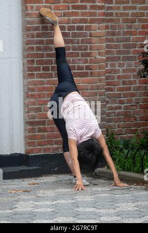 Una giovane signora agile e flessibile fa rigorosi esercizi di stretching in un parco a New York City. Foto Stock