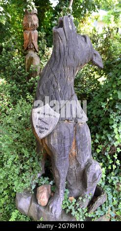 13 luglio 2021, Sassonia-Anhalt, Holzdorf-Jessen: Un lupo scolpito si trova nel 'Giardino della Foresta aperta' di circa 5,000 metri quadrati di forestere e educatore della foresta Detlef Schulze. È una delle molte figure grandi e piccole scolpite e disegnate, animali e spiegazioni nel giardino aperto, che non ha recinzione. Per 40 anni Detlef Schulze ha apprezzato la sua oasi di benessere, che può essere esplorata dai visitatori in qualsiasi momento. Foto: Waltraud Grubitzsch/dpa-Zentralbild/ZB Foto Stock