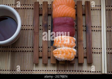 Primo piano di sushi con una ciotola di soia e bastoni su un tavolo di legno Foto Stock