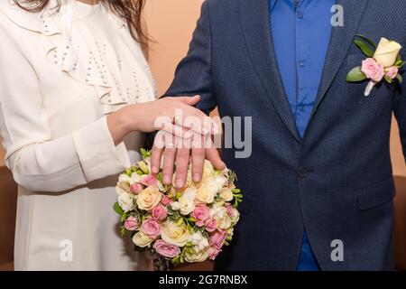 Sposa e sposo che tengono le mani mostrando i loro anelli, coppia di nozze che tiene il bouquet Foto Stock