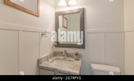 Pano interno di un bagno dipinto di bianco con lavandino e specchio Foto Stock
