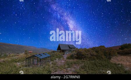 Pano costruzione di una casa con serra di vetro nel mezzo di un arbusto sotto il vibrante cielo notturno Foto Stock