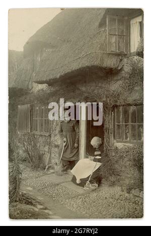 Originale inizio del 1900 's reale cartolina fotografica di saluti di case rurali e abitanti, cottage con tetto di paglia, artigianato rurale, l'uomo indossa un fumo, forse un pastore, circa 1905, Regno Unito Foto Stock