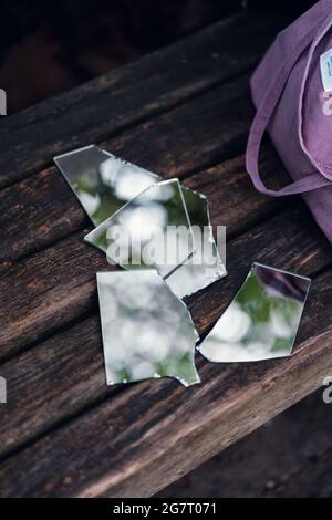 Colpo verticale di pezzi di specchio rotti su una panca di legno vicino ad una borsa viola Foto Stock