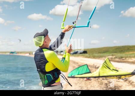 Giovane adulto caucasico fit uomo regolare kite surf board bar in sole uv protezione tuta in giornata di sole luminoso contro il cielo blu in mare o mare riva Foto Stock