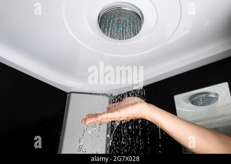 Una ragazza tiene la sua mano sopra la pressione dell'acqua da un soffione della doccia, bagno della doccia della pioggia. Foto Stock
