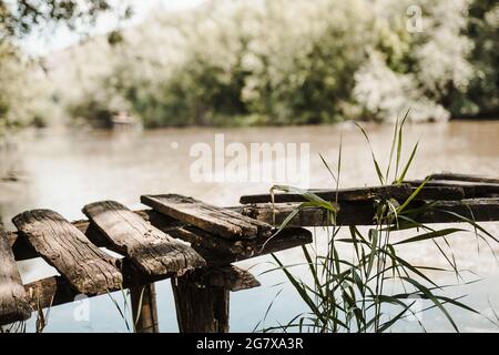 Vecchio ponte di legno danneggiato sul fiume che conduce verso la foresta Foto Stock