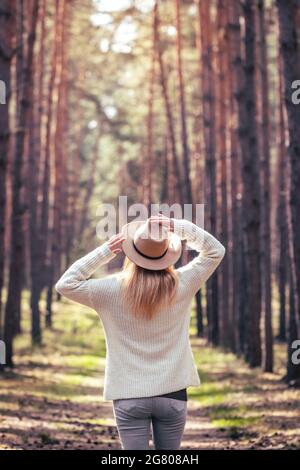 La donna gode della luce del sole e dell'aria fresca all'aperto nella natura. Boho donna che indossa cappello e maglia maglione in foresta Foto Stock