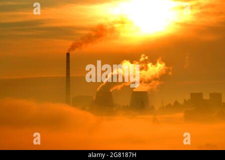 Fabbrica con camini e fumo arancio bagliore di alba Foto Stock