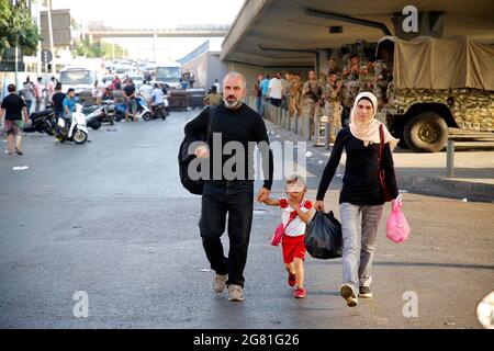 Beirut, Libano. 16 luglio 2021. Una passeggiata in famiglia vicino al luogo dove i manifestanti bloccano una strada a Beirut, Libano, il 16 luglio 2021. I manifestanti libanesi hanno chiuso le strade a Beirut per il secondo giorno di venerdì, un giorno dopo le dimissioni del primo ministro designato Saad Hariri. Hariri ha annunciato giovedì il suo fallimento nella formazione di un gabinetto, citando inconciliabili disaccordi con il presidente Michel Aoun. L’annuncio ha scatenato una dozzina di proteste in tutto il paese. Credit: Bilal Jawich/Xinhua/Alamy Live News Foto Stock