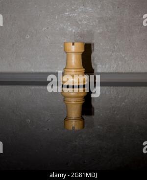 Pezzo di scacchi bianco in legno, angolo su vetro scuro specchio con fondo parete in cemento. Idea di giochi, sport e ricreazione. Concetto di intelligenza minimo. Foto Stock