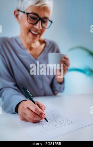 Donna anziana che risolve il puzzle sudoku Foto Stock