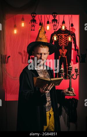 Uomo sullo sfondo dell'orrore. Sfondo decorato per Halloween. Jack-o-lanterne. Abiti e costumi di Halloween e cappelli di strega. Segreti di Foto Stock