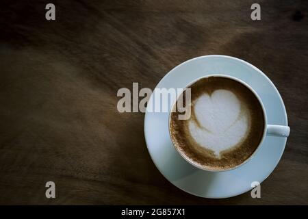 vista dall'alto di un caffè latte art nella tazza bianca su un pavimento in legno da tavolo con carta da parati Foto Stock