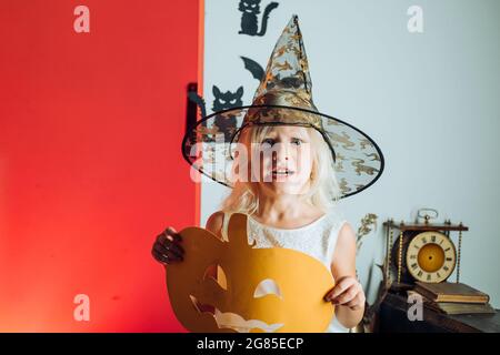 Halloween ragazza cute felice con le zucche su uno sfondo halloween. Festa di Halloween. Concetto di vacanza per bambini. Decorazione domestica di Halloween. Foto Stock