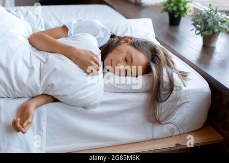 Foto di una ragazza di 10 anni che dorme sotto una coperta prima di svegliarsi. Mattina presto. Foto Stock