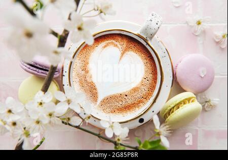 Caffè con un motivo a forma di cuore e dolci amaretti dessert uno sfondo rosa Foto Stock