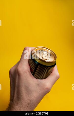 latta in una mano dell'uomo su uno sfondo giallo. Foto Stock