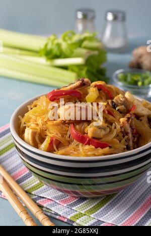 Spaghetti di riso Funchoza con frutti di mare. Pasta di cellophane, cozze, calamari e polpi, sano spuntino asiatico in una ciotola su fondo azzurro. Verti Foto Stock