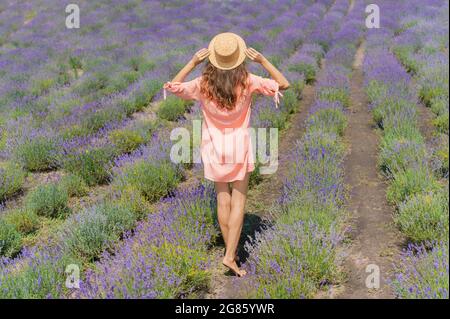 Giovane donna con abito rosa e cappello godendo la bellezza e la fragranza di un campo di lavanda in fiore Foto Stock