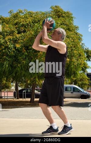 uomo maturo che gioca a basket su un campo di strada con cesto di metallo Foto Stock