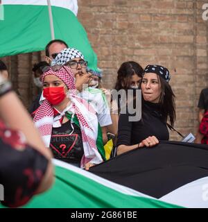 Le ragazze arabe con maschere chirurgiche sui loro volti scuotono una grande bandiera durante un incontro politico. Foto Stock