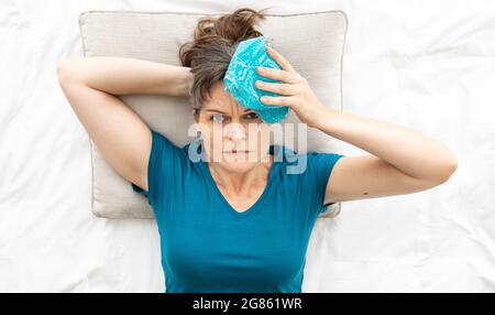 Donna di mezza età che tiene icebag sulla testa per allietare il dolore Foto Stock