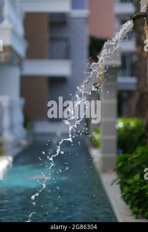 L'acqua sta sgocciando da una fontana di bronzo in stile antico, che cade in una piscina vicino a un edificio residenziale Foto Stock