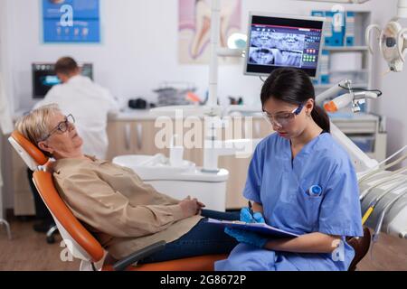 Assistente nel gabinetto dentista durante la donna anziana igiene orale controllare seduta su sedia. Donna anziana che parla con l'infermiera medica in ufficio di stomatologia circa il problema dei denti. Foto Stock