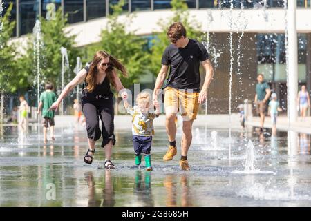 Birmingham, Regno Unito. 17 luglio 2021. Leo di due anni ha un tempo di spruzzi con mamma Emily e papà Sam nelle fontane nella Piazza del Centenario di Birmingham. Peter Lopeman/Alamy Live News Foto Stock