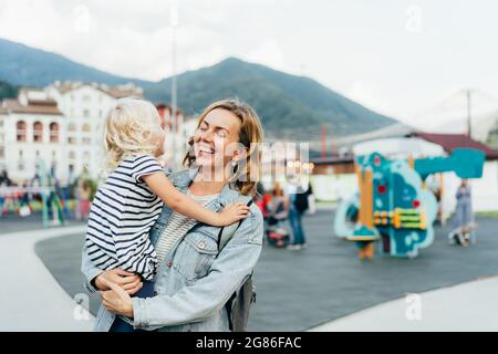 Una madre allegra abbraccia la figlia e ride mentre la tiene fra le braccia. Felici e sincere emozioni. Foto Stock