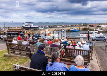 I visitatori possono ammirare la vista sul porto di Seahouses, con barche che portano i turisti alle vicine Isole Farne sulla costa del Northumberland, in Inghilterra. Foto Stock