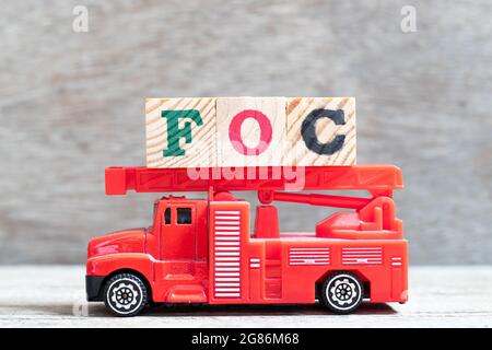 Il camion rosso del fuoco tiene il blocco della lettera in parola FOC (abbreviazione di libero di carica) su sfondo di legno Foto Stock