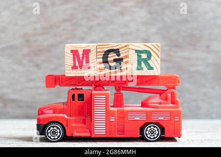 Il camion fuoco rosso tiene il blocco di lettera in parola mgr (abbreviazione del gestore) su sfondo di legno Foto Stock