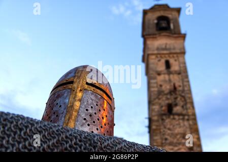 Primo piano di un casco poggiato su una catena con un campanile romanico sullo sfondo Foto Stock